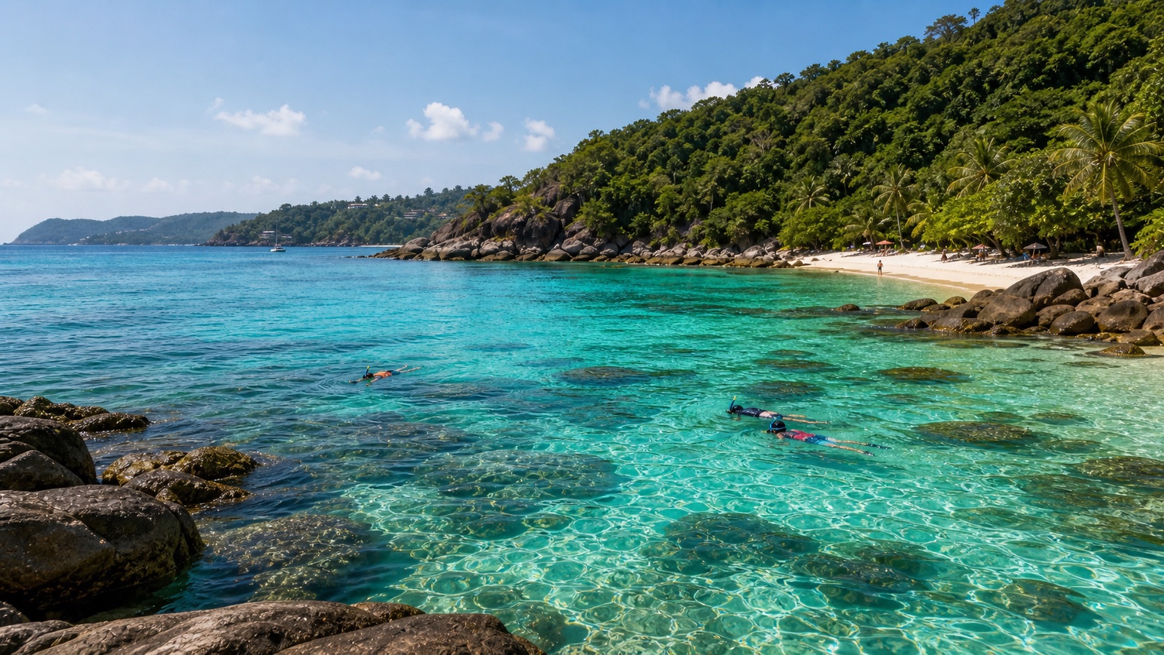 Snorkelers in clear water near a rocky Phuket beach headland